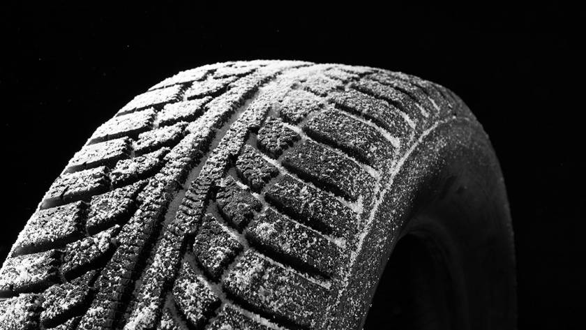Close-up of a winter tire covered in snow, showing deep tread patterns designed for traction on icy roads.