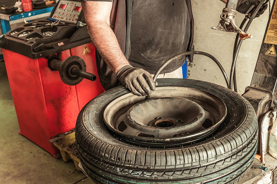Auto technician using tire mounting equipment to install a new tire onto a wheel rim inside a repair shop.